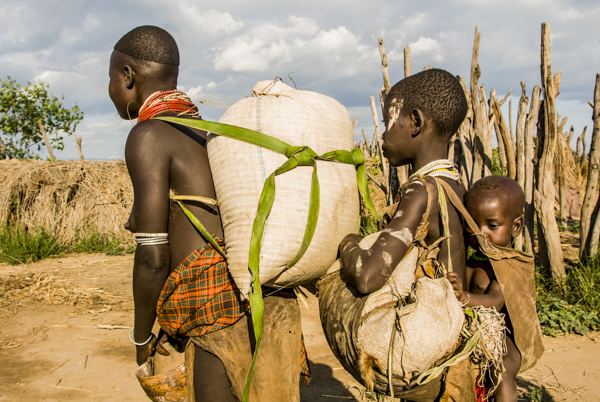 Ethiopia:  Lower Omo River Basin, Kotrouru, a Karo village, woman with empty gerrycan and young girl  both carrying sacks of sorghum back to their home