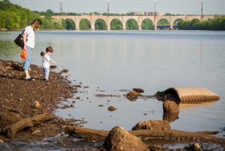 USA:  New Jersey, Highland Park, along River Road, view from banks of Raritan River of New Brunswick and Albany St Bridge on other side, spillway for runoff in foreground, woman and child exploring shoreline
